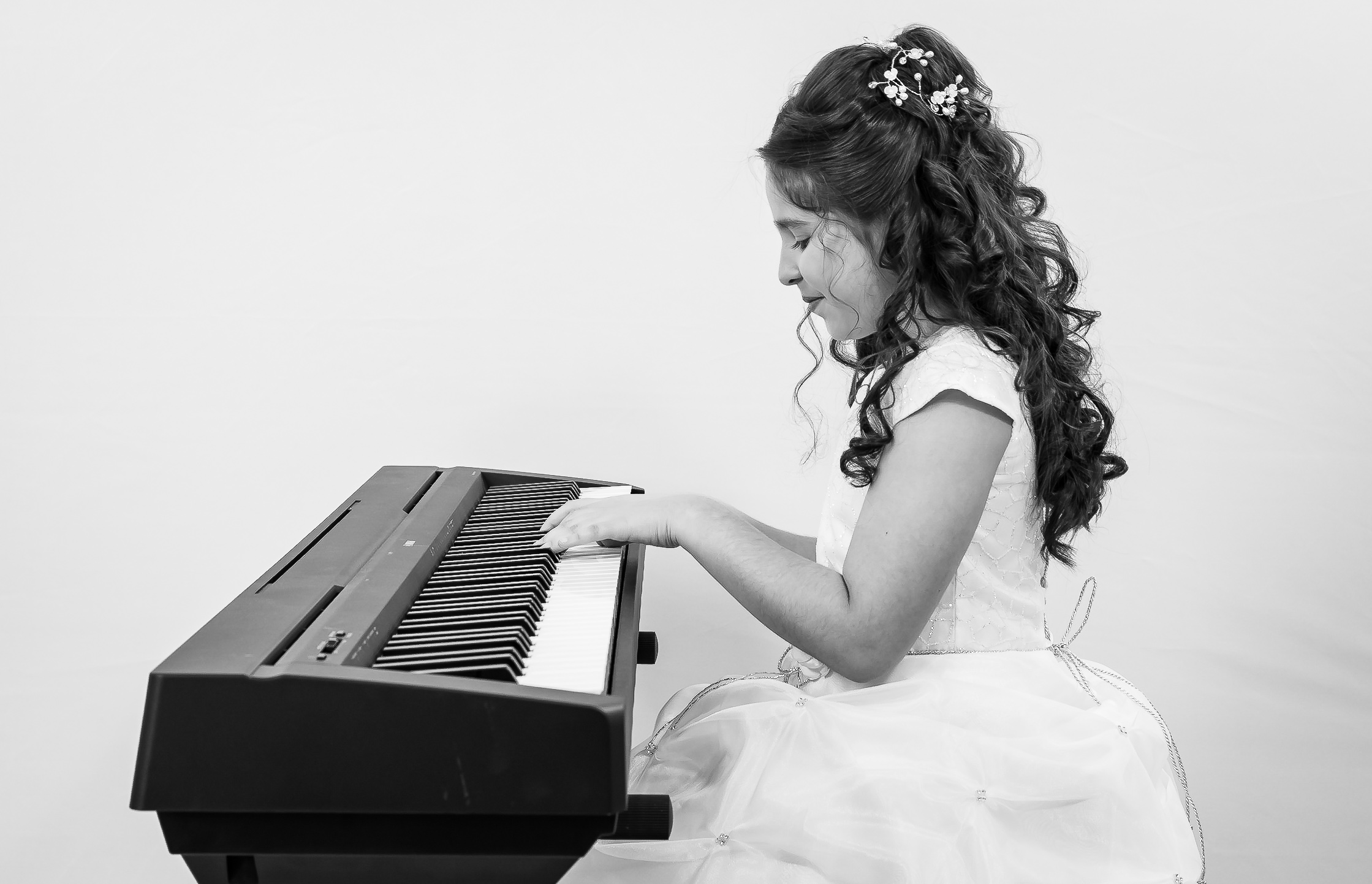 Jeune fille en robe de première communion jouant du piano, vue de profil