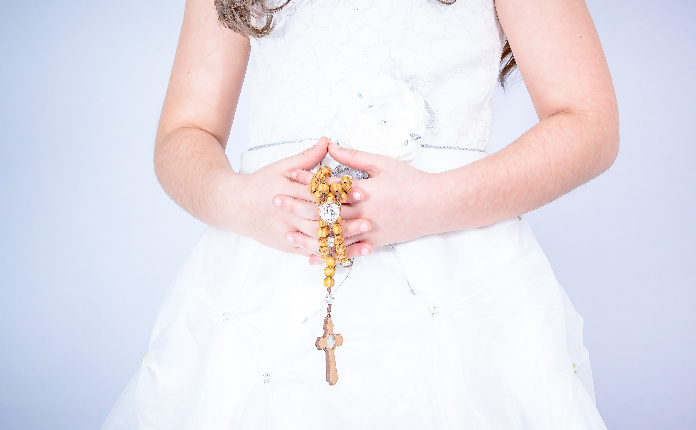 Gros plan sur des mains jointes tenant un chapelet en bois, robe de communion