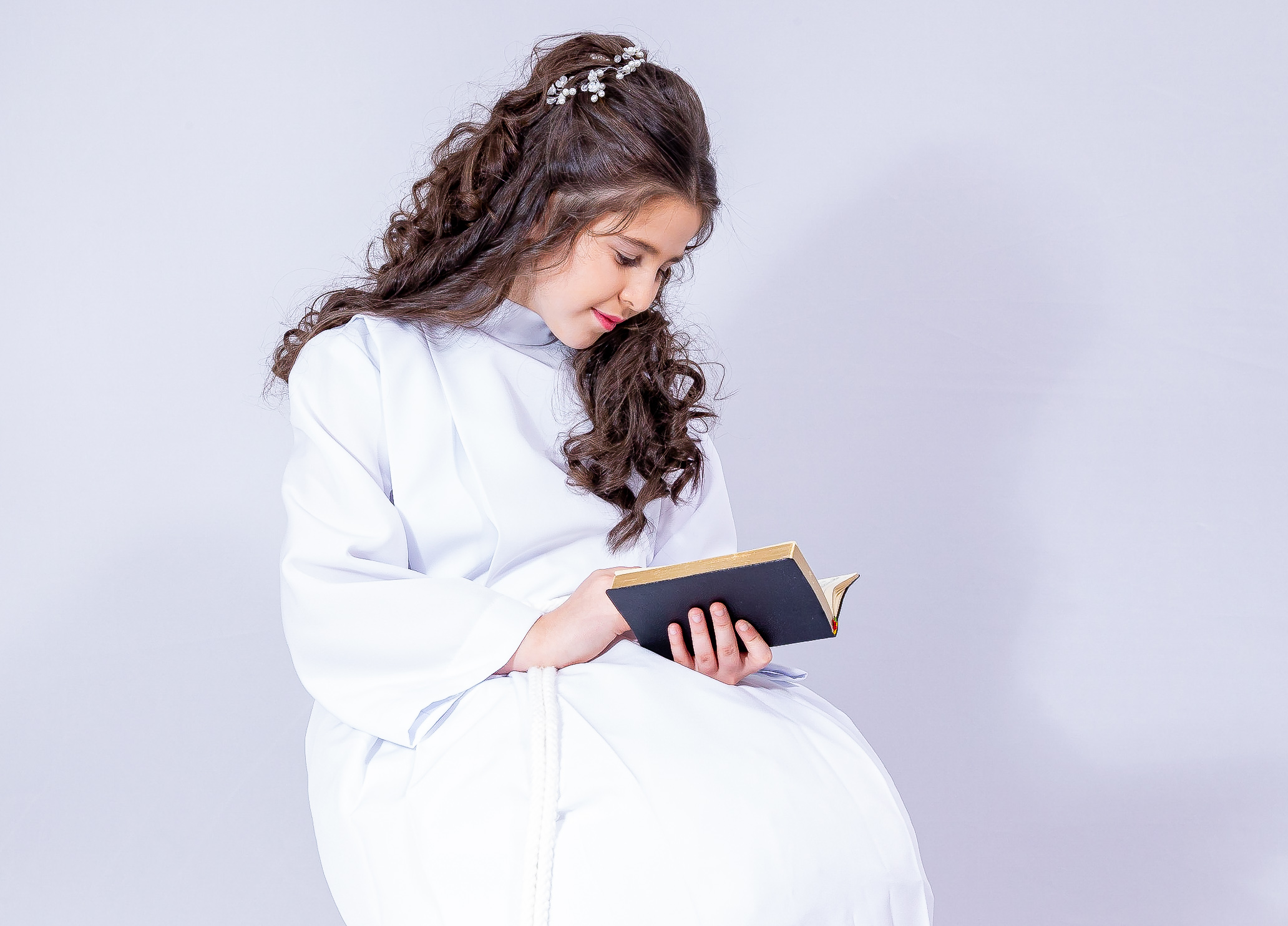 Jeune fille en aube blanche, vue de profil, lisant un livre en lumière douce