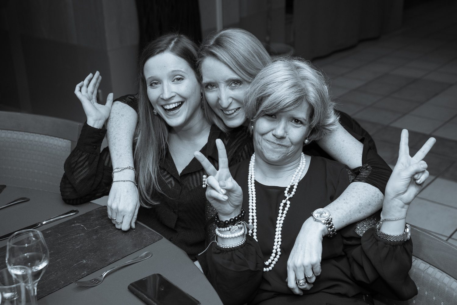 Trois femmes souriantes à table, signes de victoire