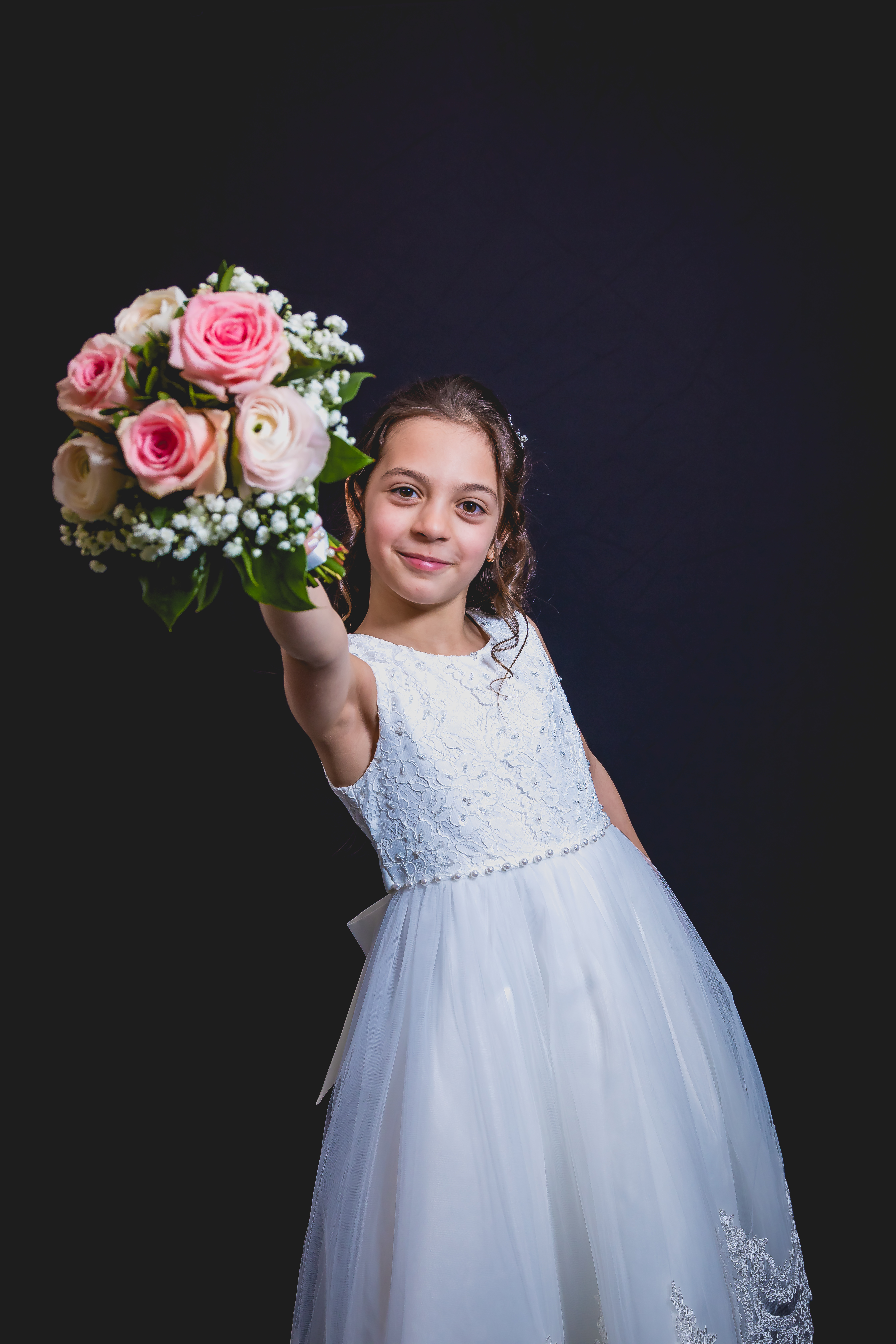 Jeune fille en robe de communion tendant un bouquet de roses roses vers l’objectif, sourire