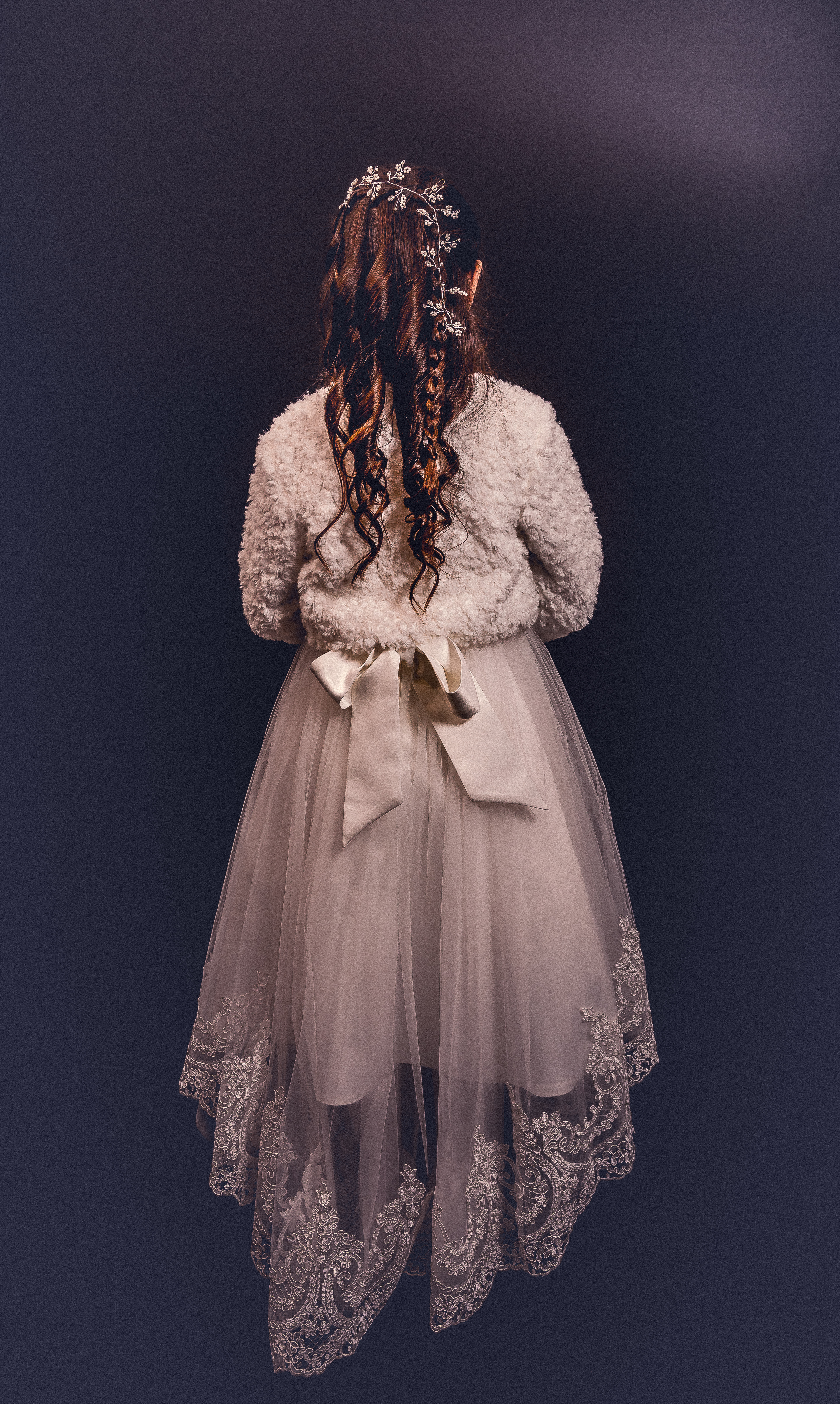 Jeune fille en robe de communion vue de dos, cheveux tressés ornés de perles
